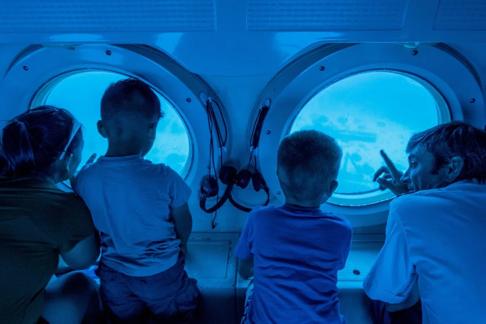 Four children kneeling at two round submarine portholes looking into blue water