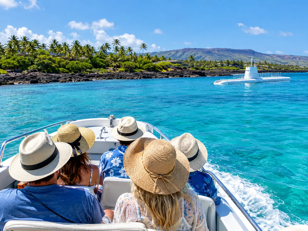 Tourists in sun hats on a small shuttle boat crossing turquoise water toward a white submarine